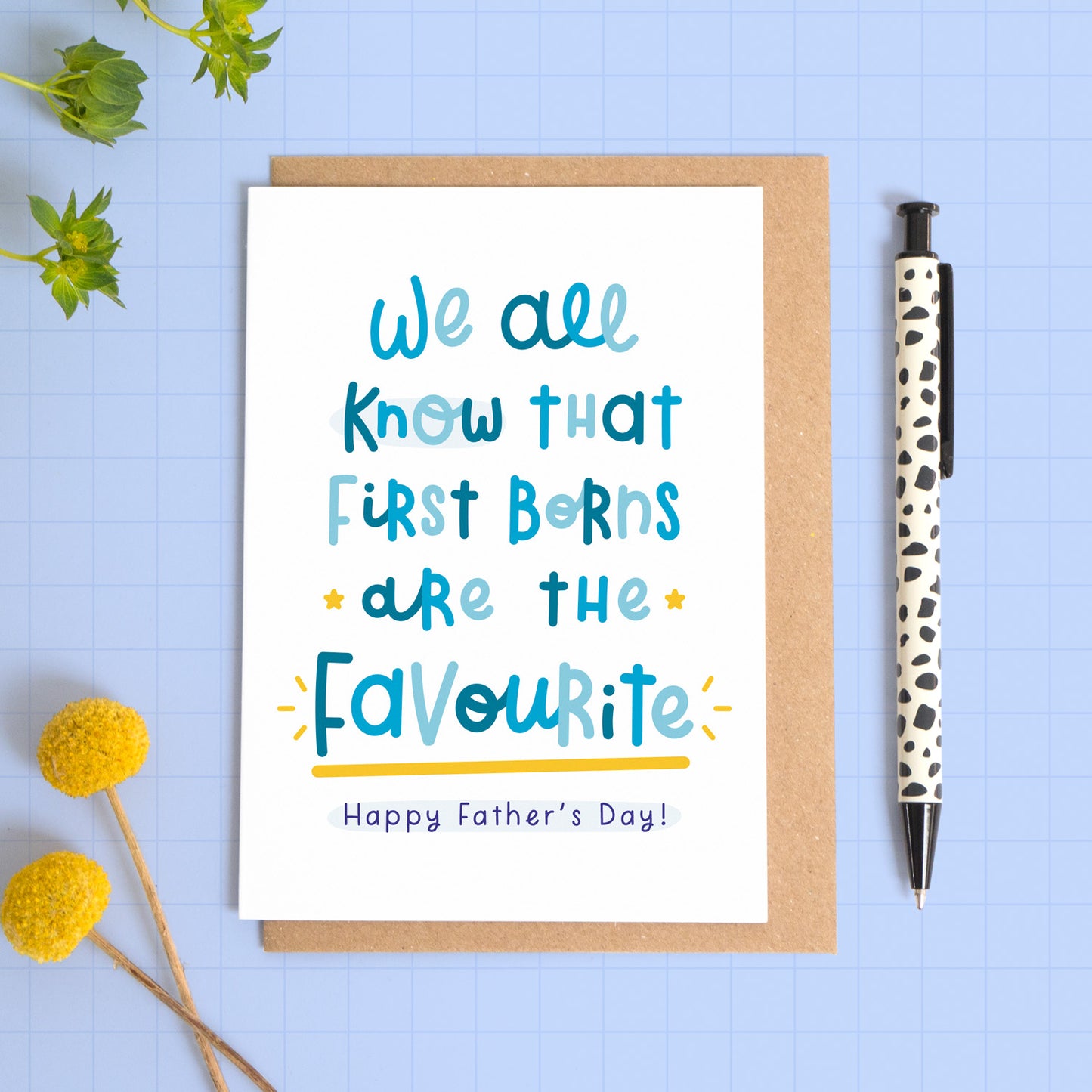 A funny favourite child card to put an end to sibling rivalry! This image shows the father's day card with text on the front reading 'we all know that first borns are the favourite. Happy Father's day!' The text is in varying tones of blue and the card itself is laid on top of a kraft brown envelope. The card has been photographed on a blue background with a pen and flowers for props.