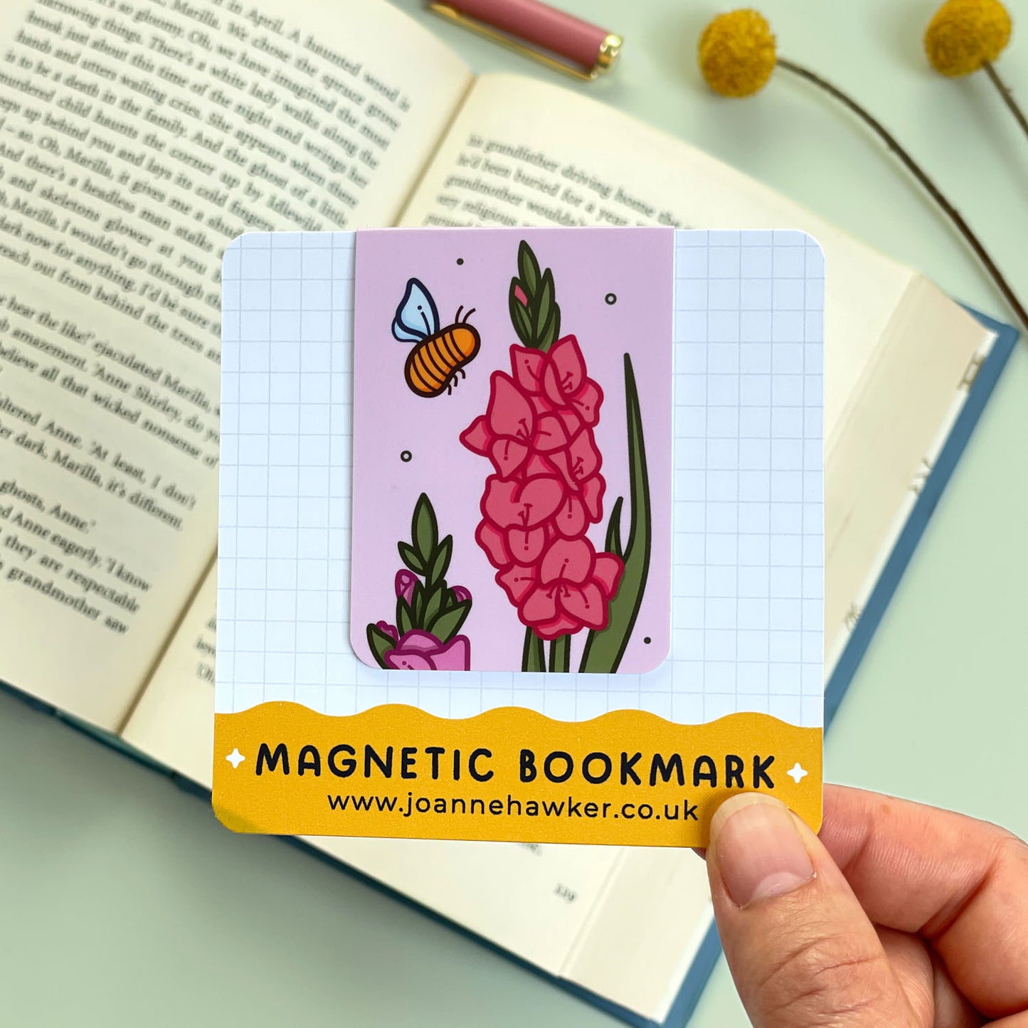 Magnetic bookmark with floral gladiolus design held over an open book