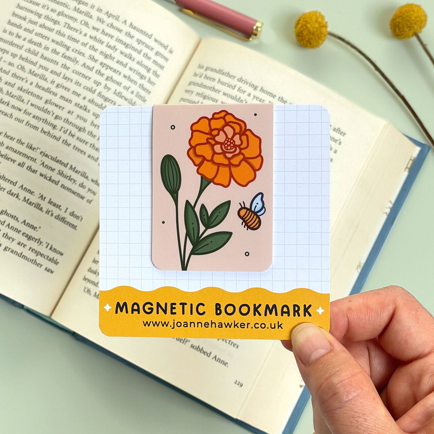 Magnetic bookmark with orange floral marigold design held over an open book