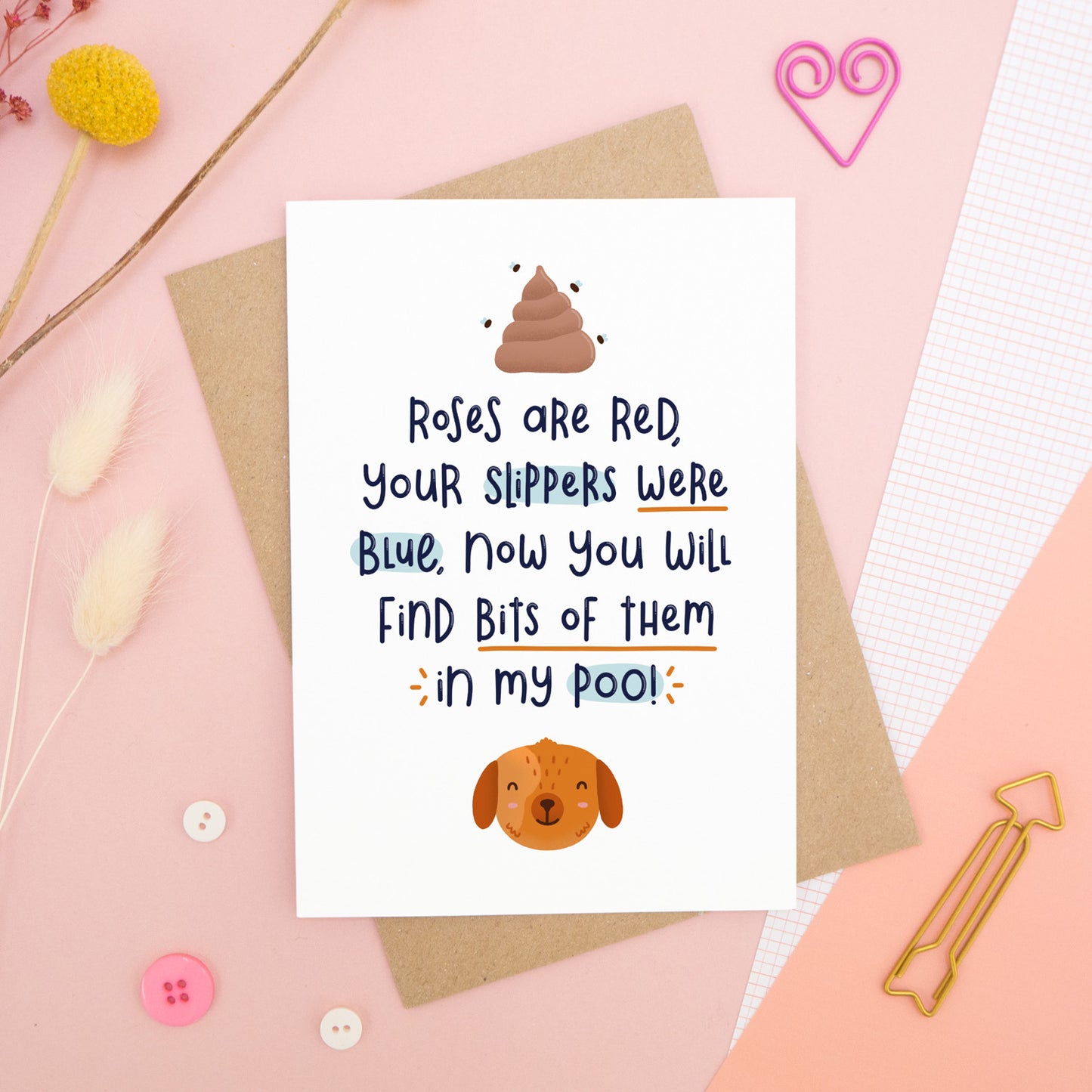 A Valentine’s ‘from the dog’ card featuring a ‘roses are red’ rhyme, photographed on a pink background with floral props, paper clips, and buttons.