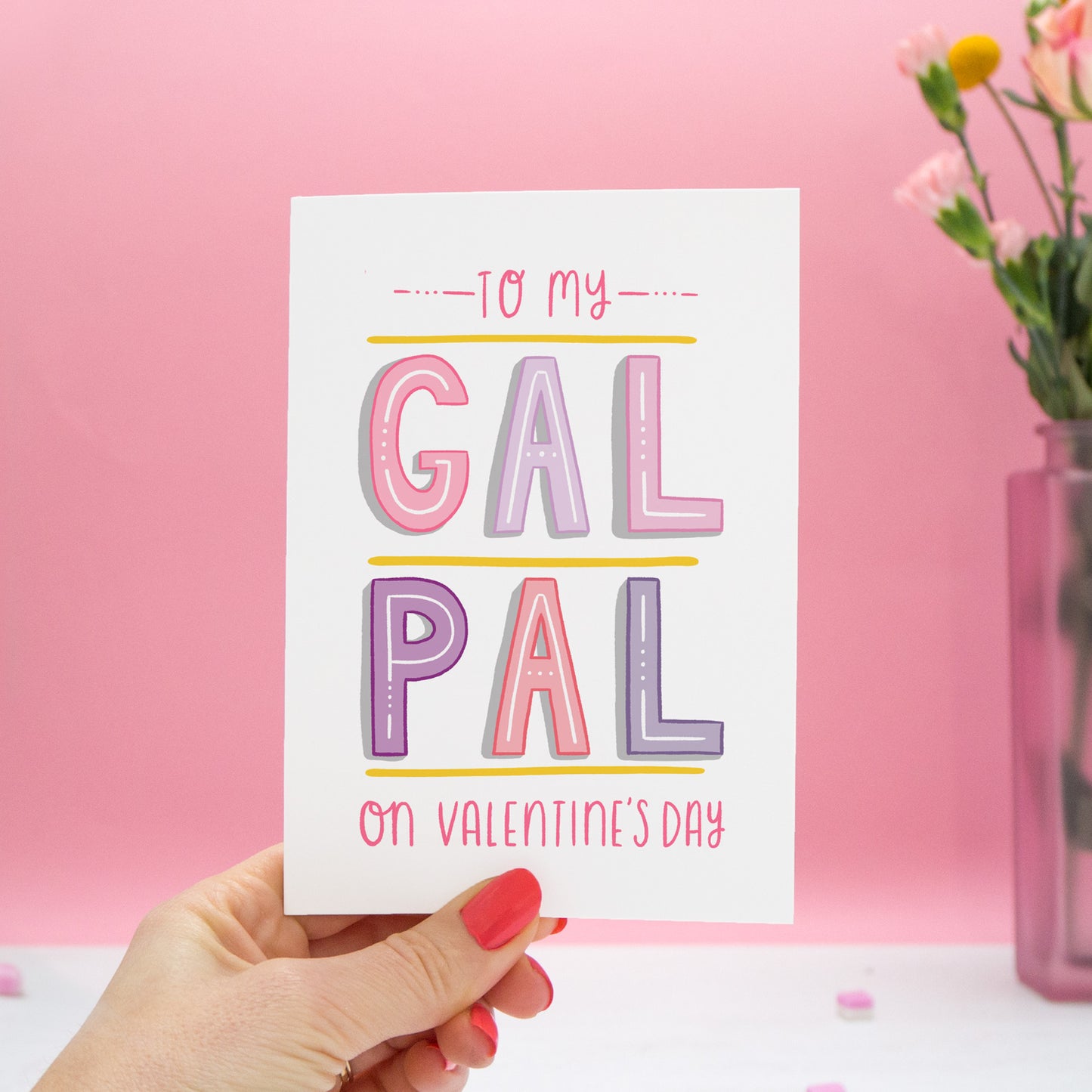 To my Gal Pal on Valentine's Day. A friendship card designed for Valentine's or Galentine's day! The image features my hand lettered card held in my left hand and with a vase of roses on a pink background