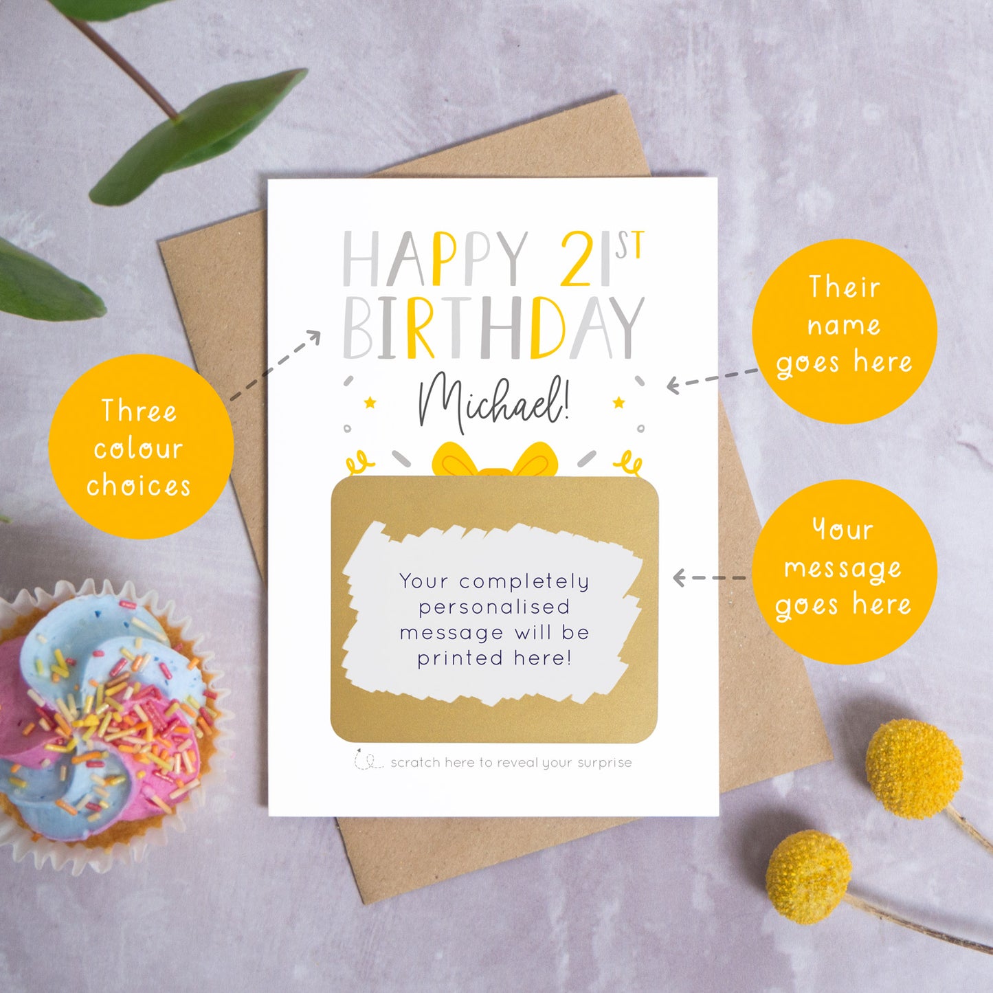 A personalised happy 21st birthday scratch card in grey that has been photographed on a grey background with foliage and a cupcake. There are also orange circles laid over the top of this image with arrows pointing to the areas that can be customised. In this instance they point to the name, the colour choices and the personalised scratch off message.