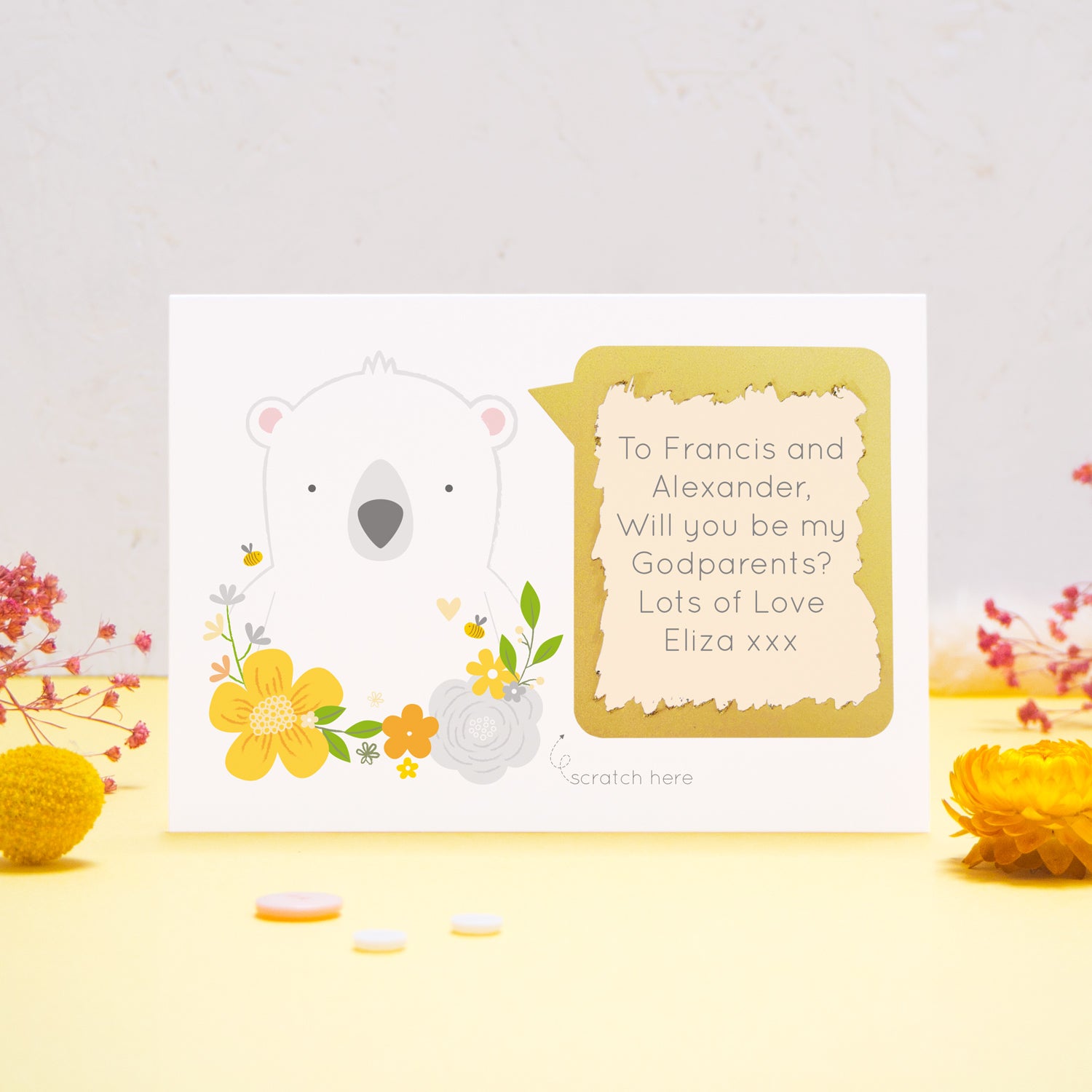A personalised will you be my godparents scratch card featuring a white bear, yellow flowers and a peach text box. This has been shot on a yellow and grey background with flowers. The gold panel has been scratched away to reveal the message.