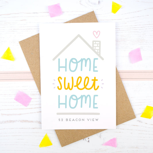 Home Sweet Home is a personalised card featuring the property number and road name. This version has a grey roof, a heart coming from the chimney and has 'home sweet home' in blue and orange.
