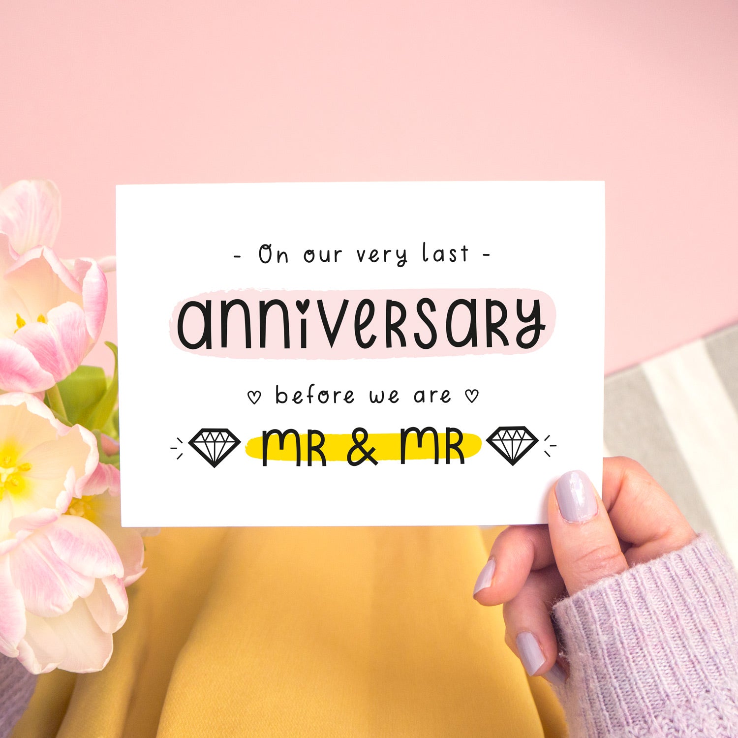 A last anniversary or Valentine’s card photographed on a pink background with pink tulip flowers, a grey and white stripe rug and yellow fabric. This image shows the last anniversary option with the Mr & Mr wording. The text is black and there are pops of yellow and pink behind key words.