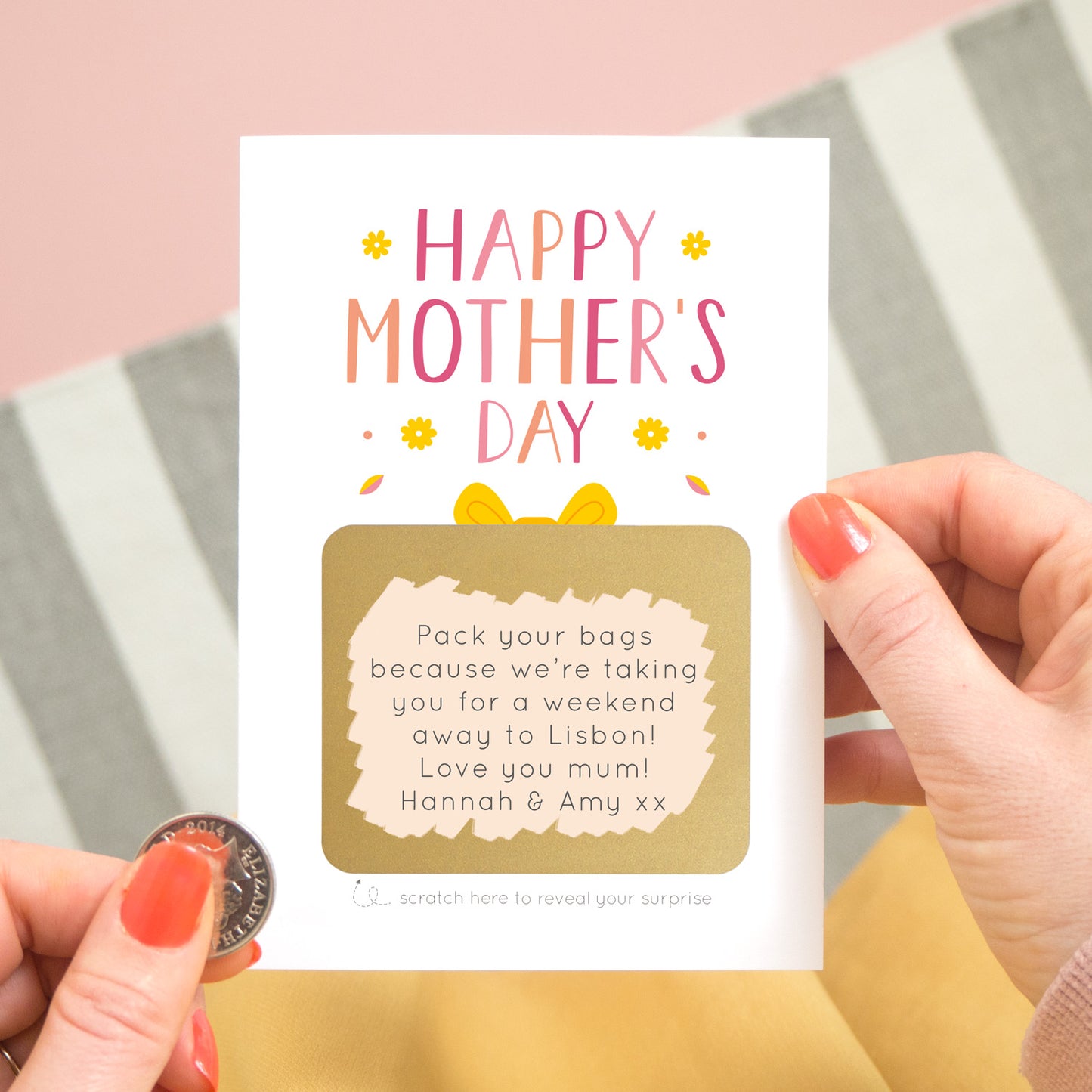 A mother’s day present scratch card held over a grey and white striped rug with a pink background in the corner. The card reads ‘Happy Mother’s day’ and the gold present has been scratched off with a coin to reveal a custom message to a mum. This card is in the pink and peach colour palette.