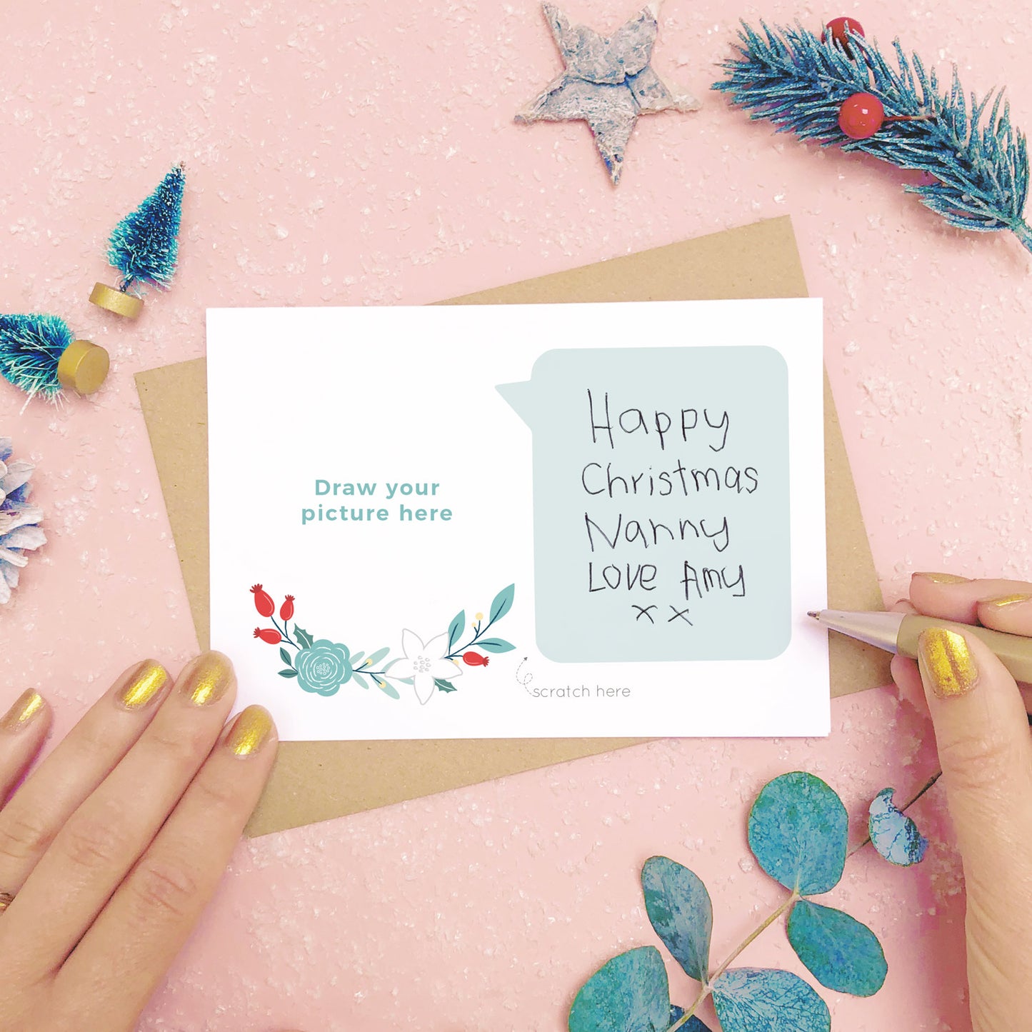 A draw your own scratch card showing where to hand write the message for scratching off. Shot on pink with snow and greenery.