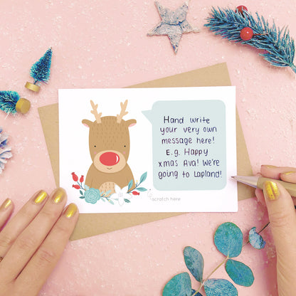A personalised red nose reindeer scratch card showing where to write the hand written message. Shot on a pink background with grey and green festive props.