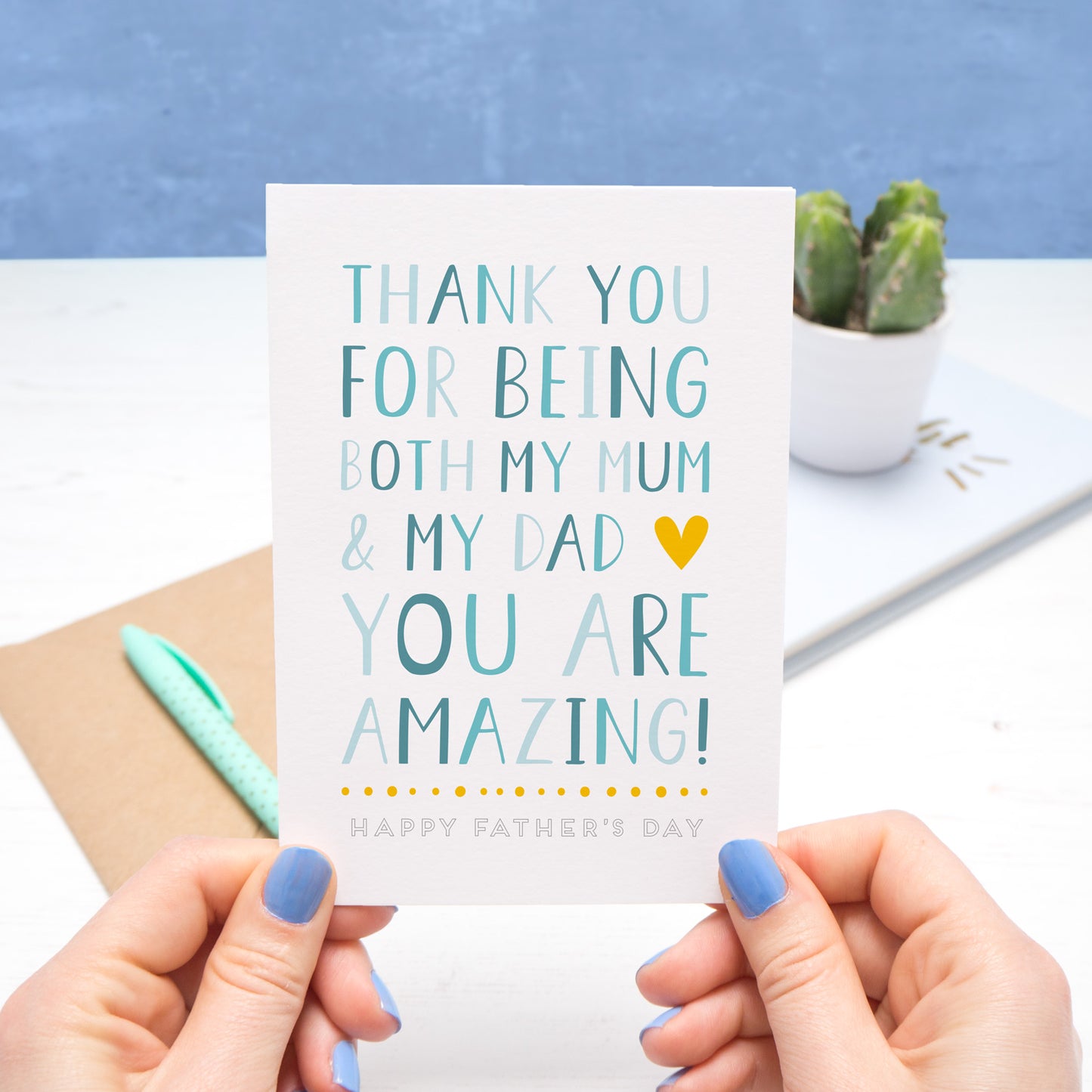 A card for the amazing single parent who plays the role of mum and dad. This image features the card being held by Joanne Hawker on a white and blue background. The card features blue text with a yellow heart.