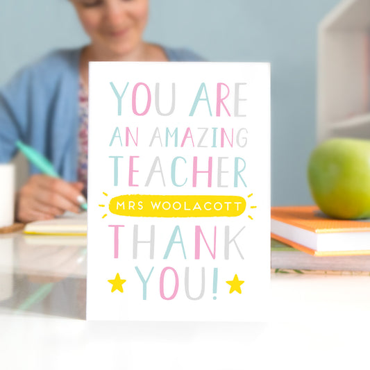 A personalised thank you teacher card that reads 'you are an amazing teacher [insert name of teacher] thank you! In pink, blue, grey and a pop of yellow
