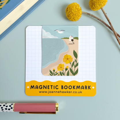 The Burnham on Sea magnetic bookmark on it's backing card set on a blue background with a yellow flower and polka dot pen.