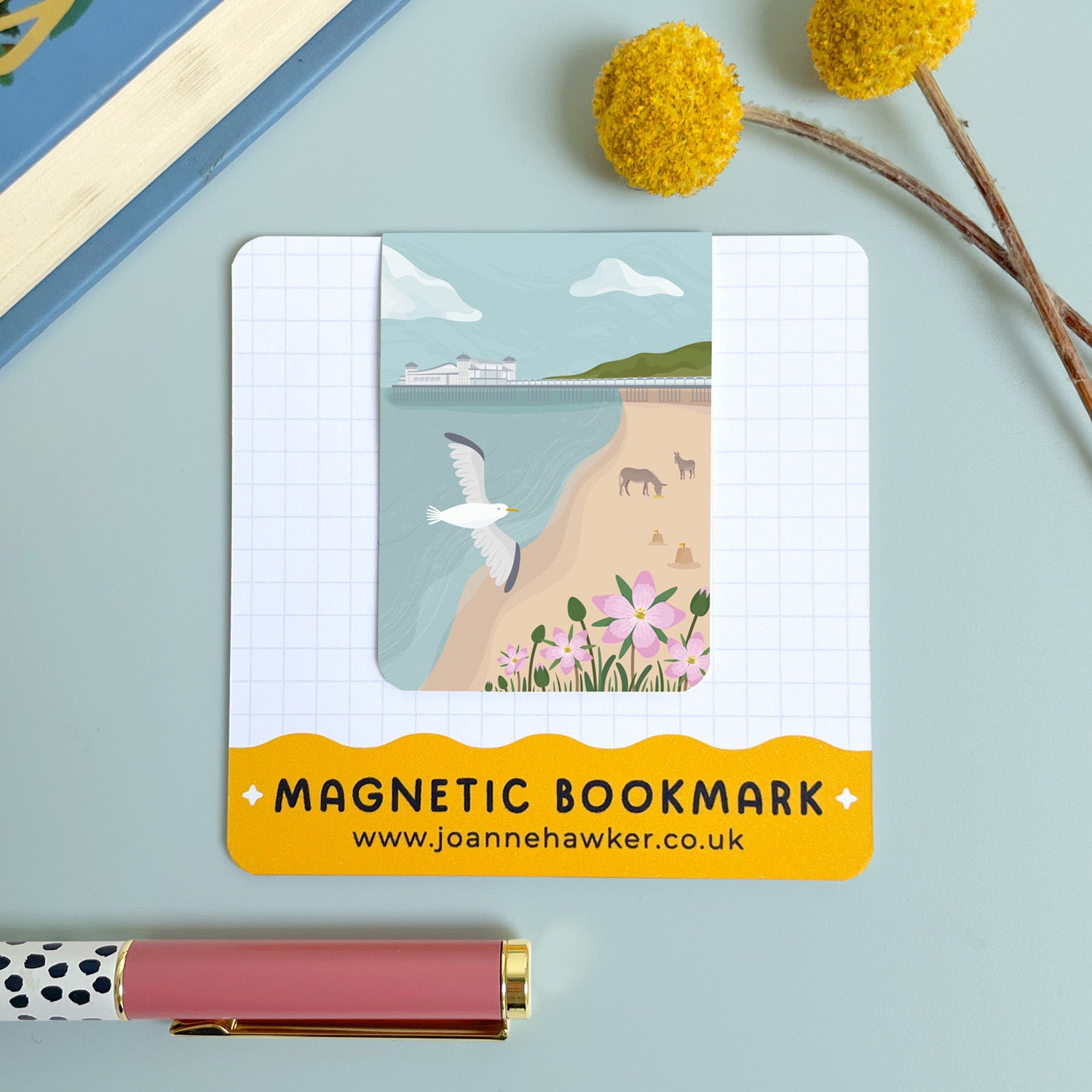 The Weston-Super-Mare magnetic bookmark on the backing card set on a blue background with yellow flowers and polka dot pen.