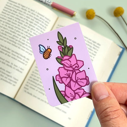 A floral gladiolus bookmark with pink flowers and a bee held over an open book