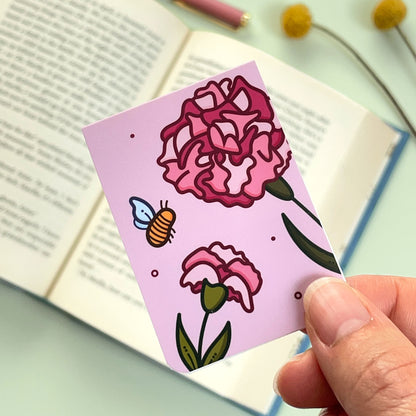 A floral carnation bookmark with pink flowers and a bee held over an open book