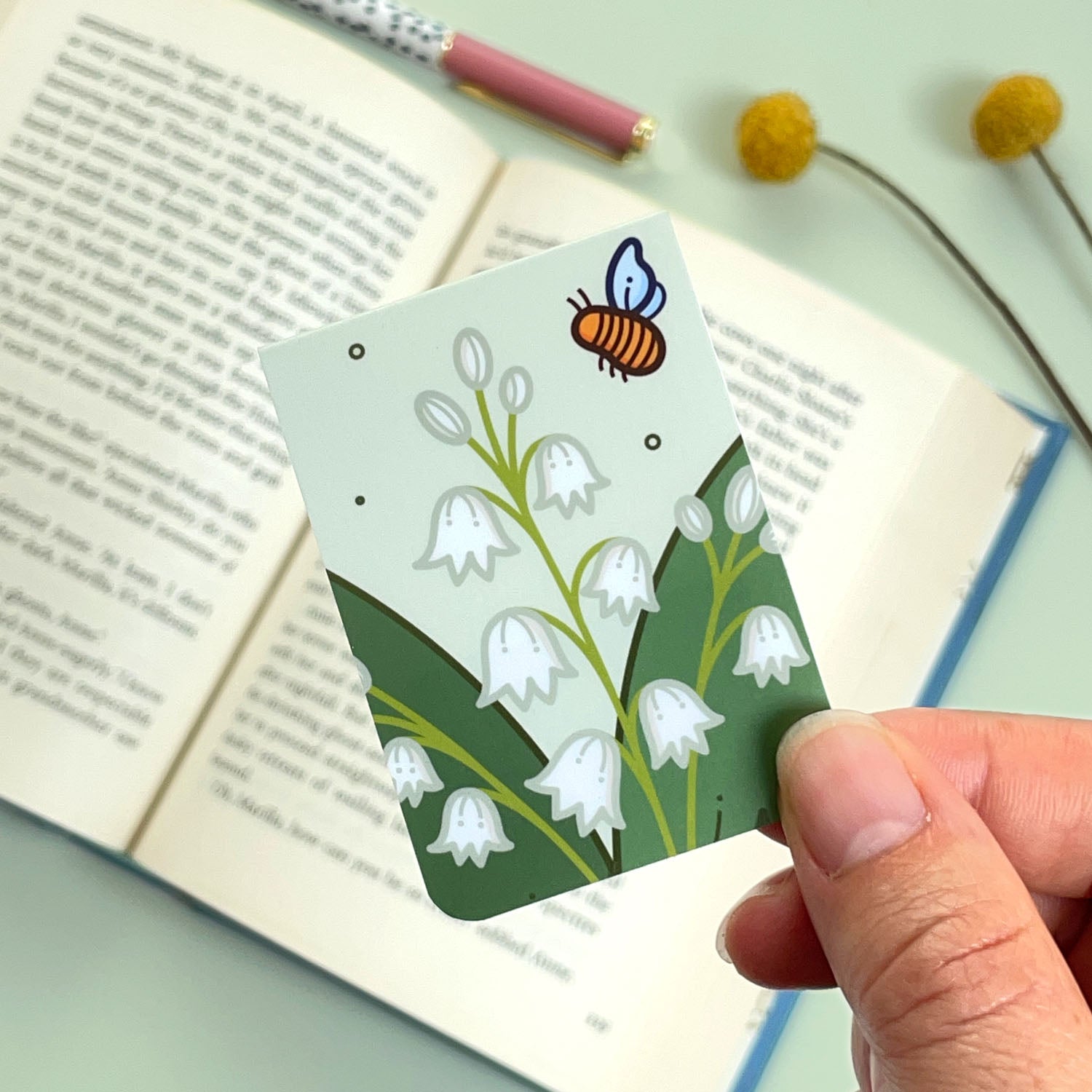 Bookmark with floral lily of the valley design held over an open book