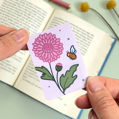 A floral chrysanthemum bookmark with pink flowers and a bee held over an open book
