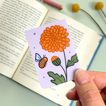 The reverse side of the floral chrysanthemum bookmark with orange flowers and a bee held over an open book