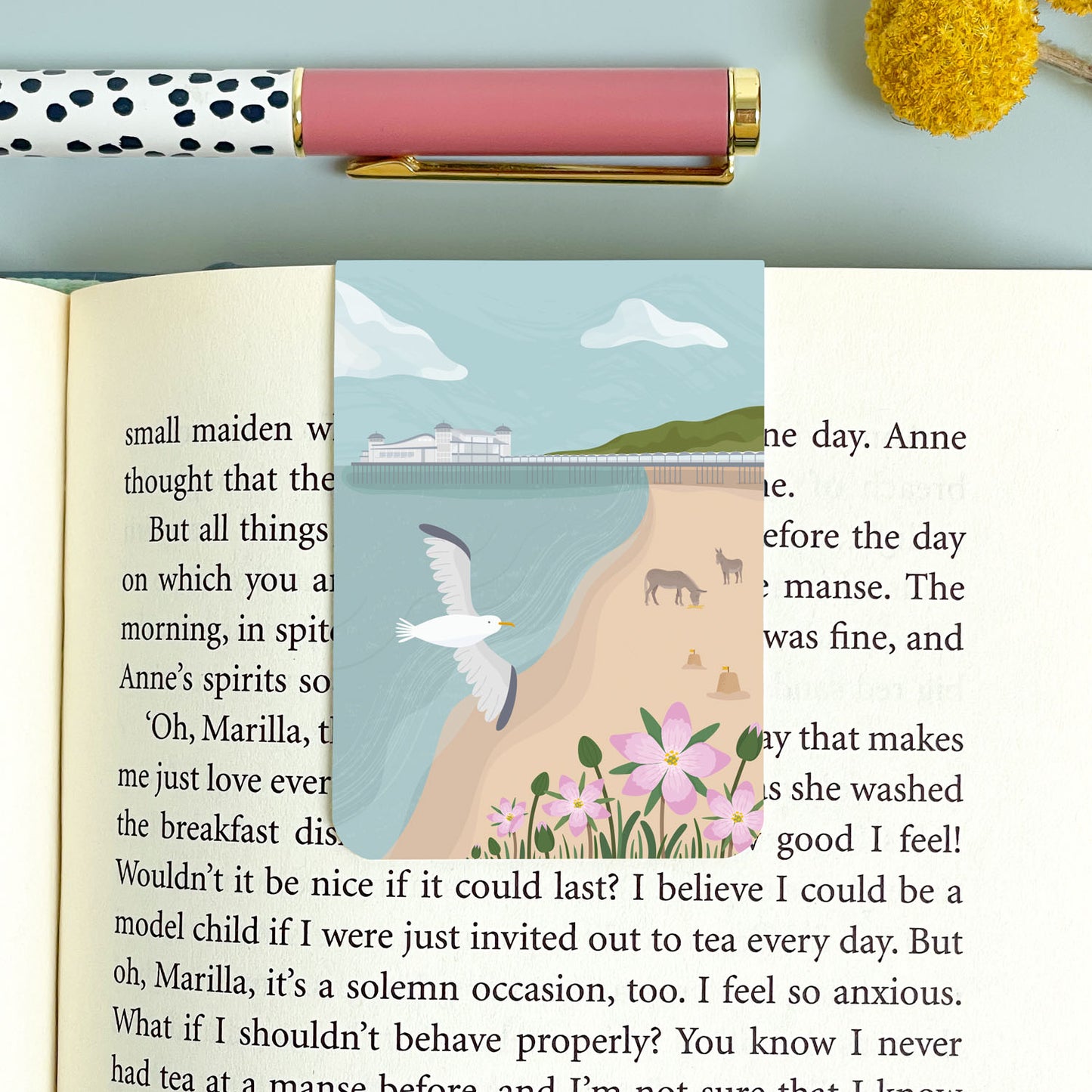 The Weston-Super-Mare bookmark with a seagull, donkeys and the grand pier. This magnetic bookmark is placed on the book on top of a blue background and polka dot pen.