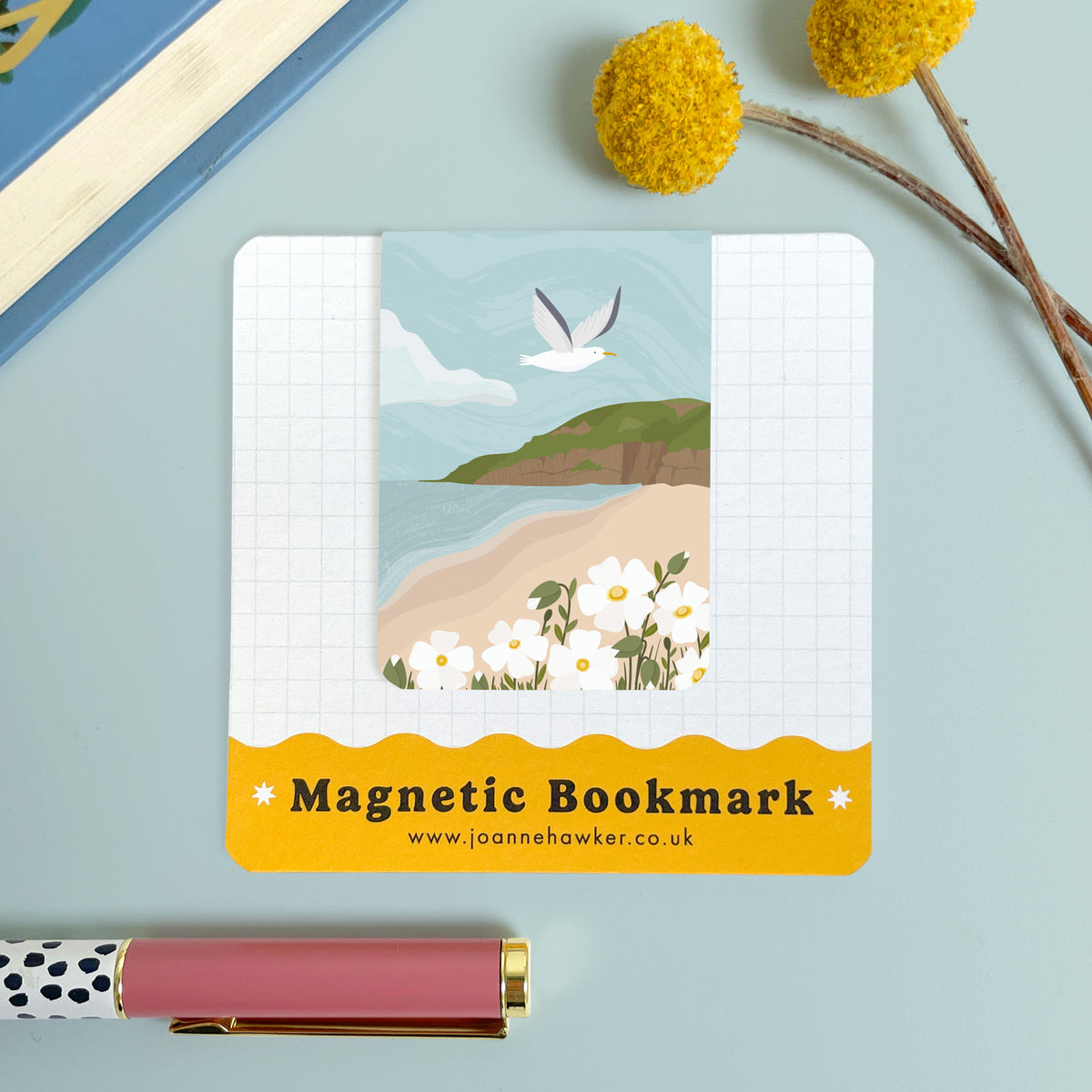 The Brean Down magnetic bookmark on it's backing card set on a blue background with a yellow flower and polka dot pen.