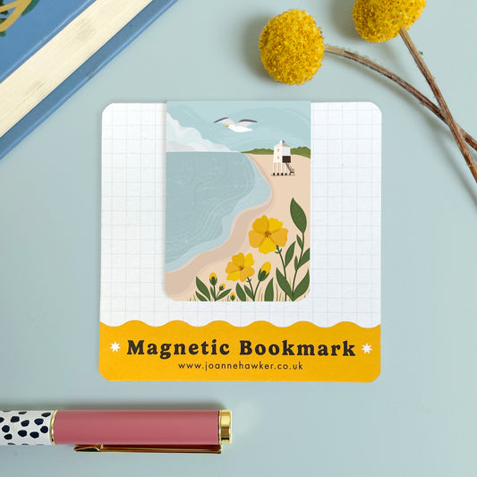 The Burnham on Sea magnetic bookmark on it's backing card set on a blue background with a yellow flower and polka dot pen.