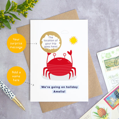 A seaside holiday reveal scratch card featuring a friendly red crab holding the scratch panel. The gold panel has been scratched off to reveal the area that your destination will be printed. Beneath the crab illustration the text reads: “we’re going on holiday Amelia”. This card has been shot on a grey background with a pen and foliage. To the left are two circles which point to the areas that can be customised. These are the name and the location of the holiday.