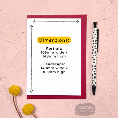 This image shows the dimensions of the greeting card. The card has a red envelope and it has been photographed on a pink background next to yellow flowers and a pen for scale.