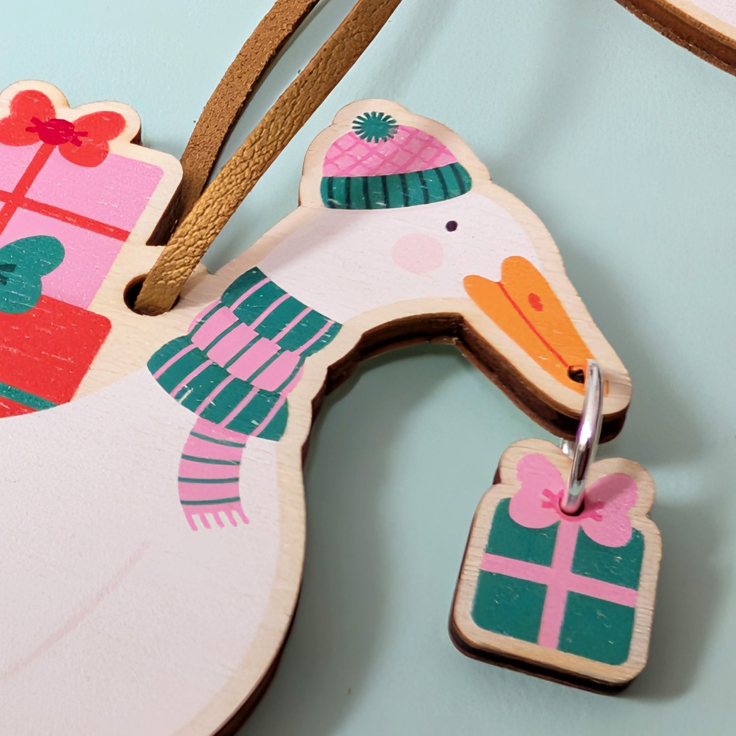 Wooden duck-shaped Christmas decoration with a scarf and present on a light blue background