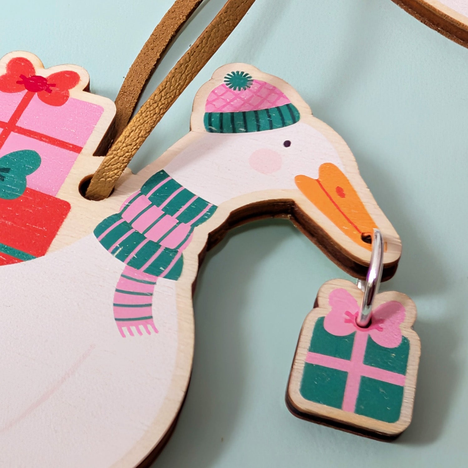Wooden duck-shaped Christmas decoration with a scarf and present on a light blue background