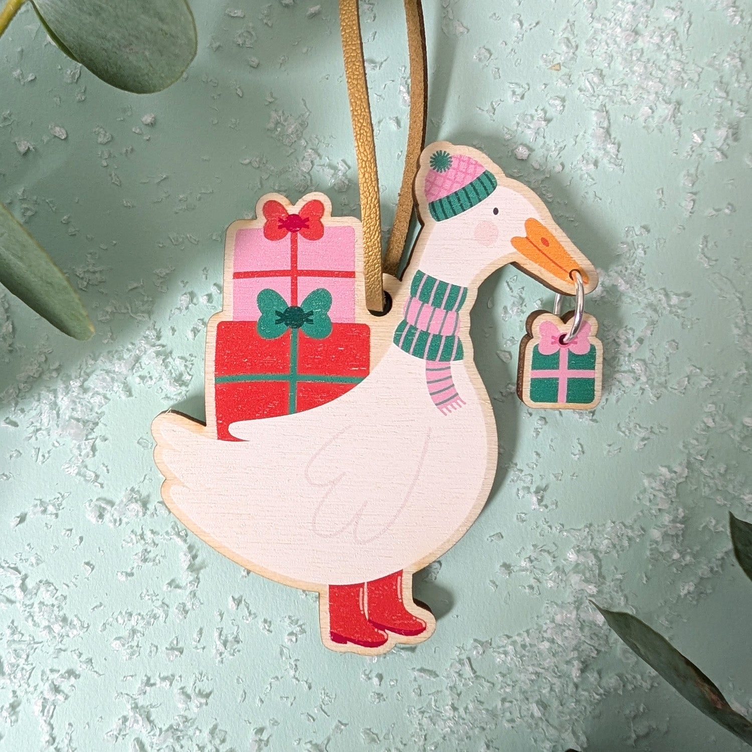 Decorative goose ornament with gift box and scarf on a textured light blue background