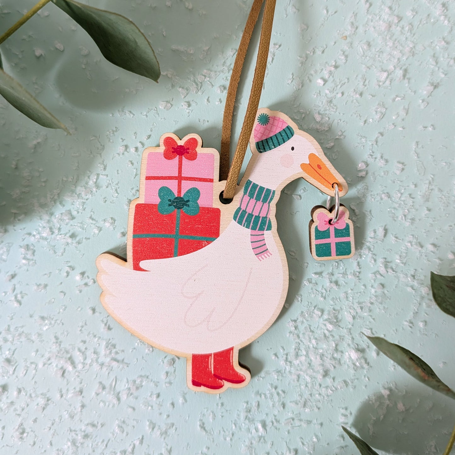 Wooden decorative duck ornament with present and scarf on a snow textured surface