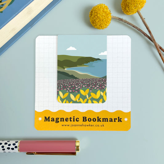 The Exmoor bookmark featuring a view across Bossington Hill to the Bristol Channel. The backing card is laid on a light blue surface with a pen and pom pom flowers.