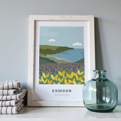 Exmoor National Park art print in a white frame on a light grey background with a pile of cloths and blue vase.
