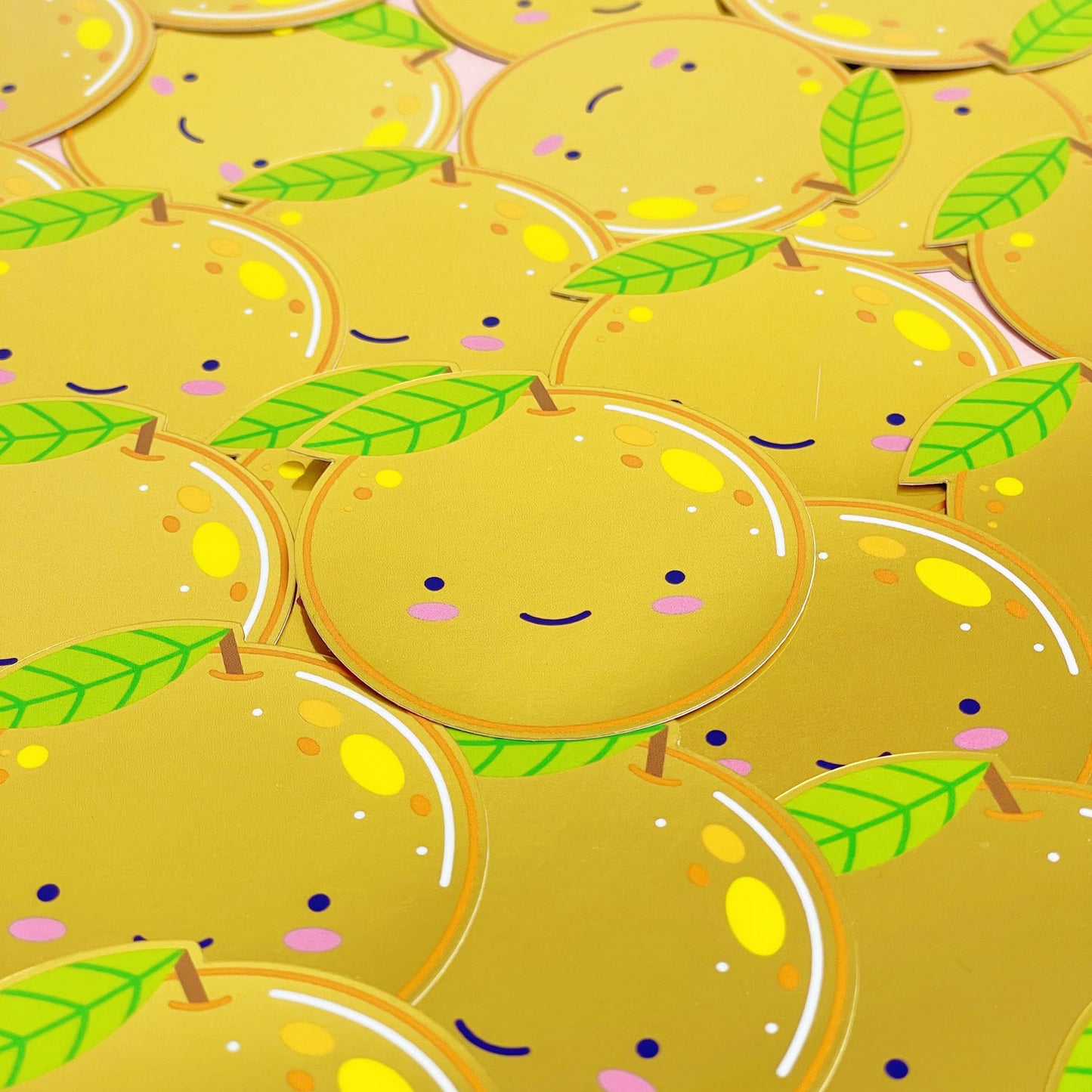 A pile of shiny mirror effect gold stickers featuring a smiling orange. The surface is covered with dozens of the same design.