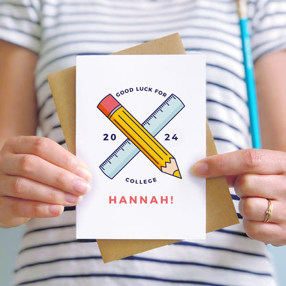 Good luck for college personalised back to school card featuring a pencil, ruler and the young persons name. The card is being held by a person in a stripy white and blue t-shirt.