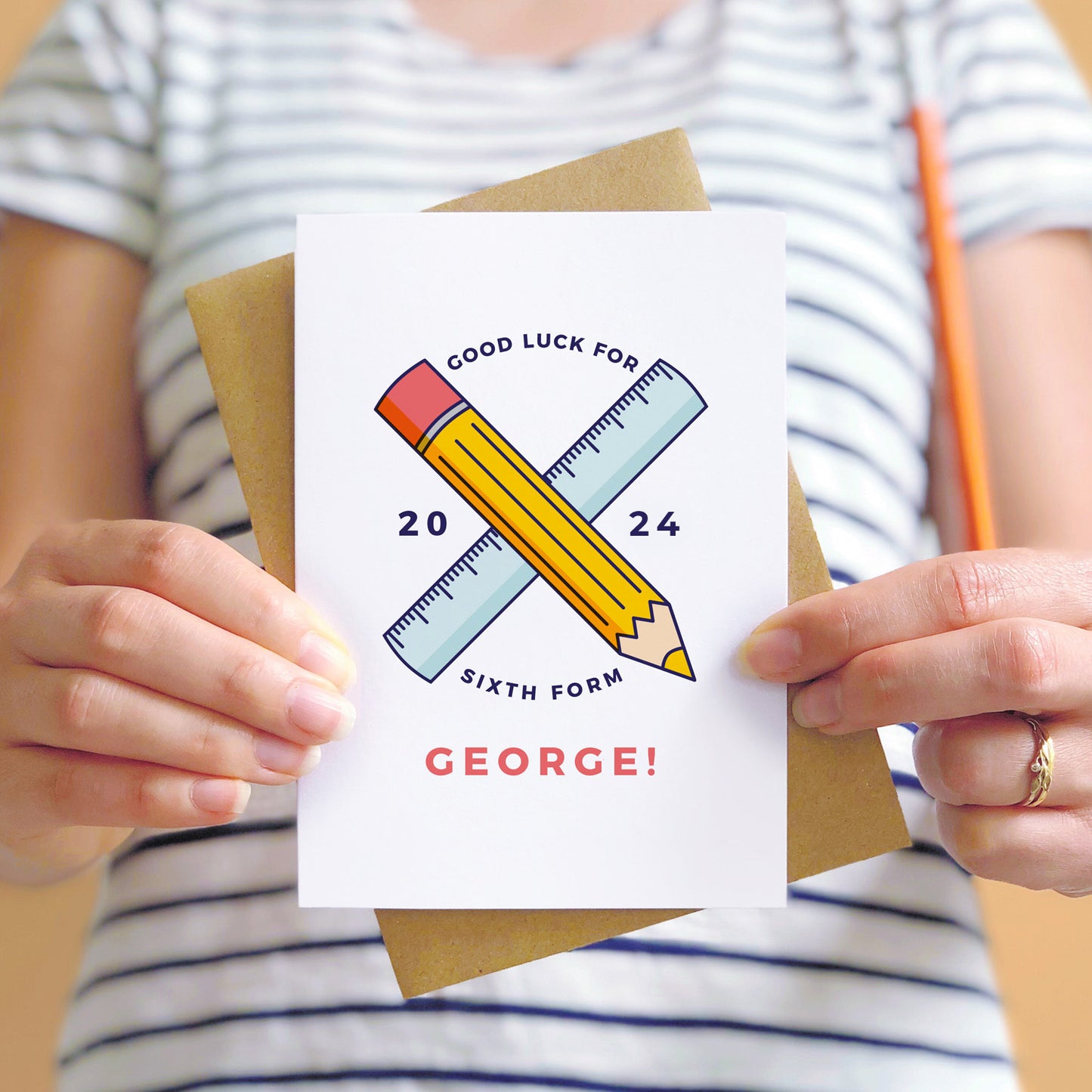 Good luck for 6th form personalised back to school card featuring a pencil, ruler and the young persons name. The card is being held by a person in a stripy white and blue t-shirt.
