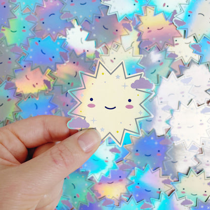 A shiny iridescent holographic vinyl sticker featuring a smiling starburst being held over a pile of stickers of the same design