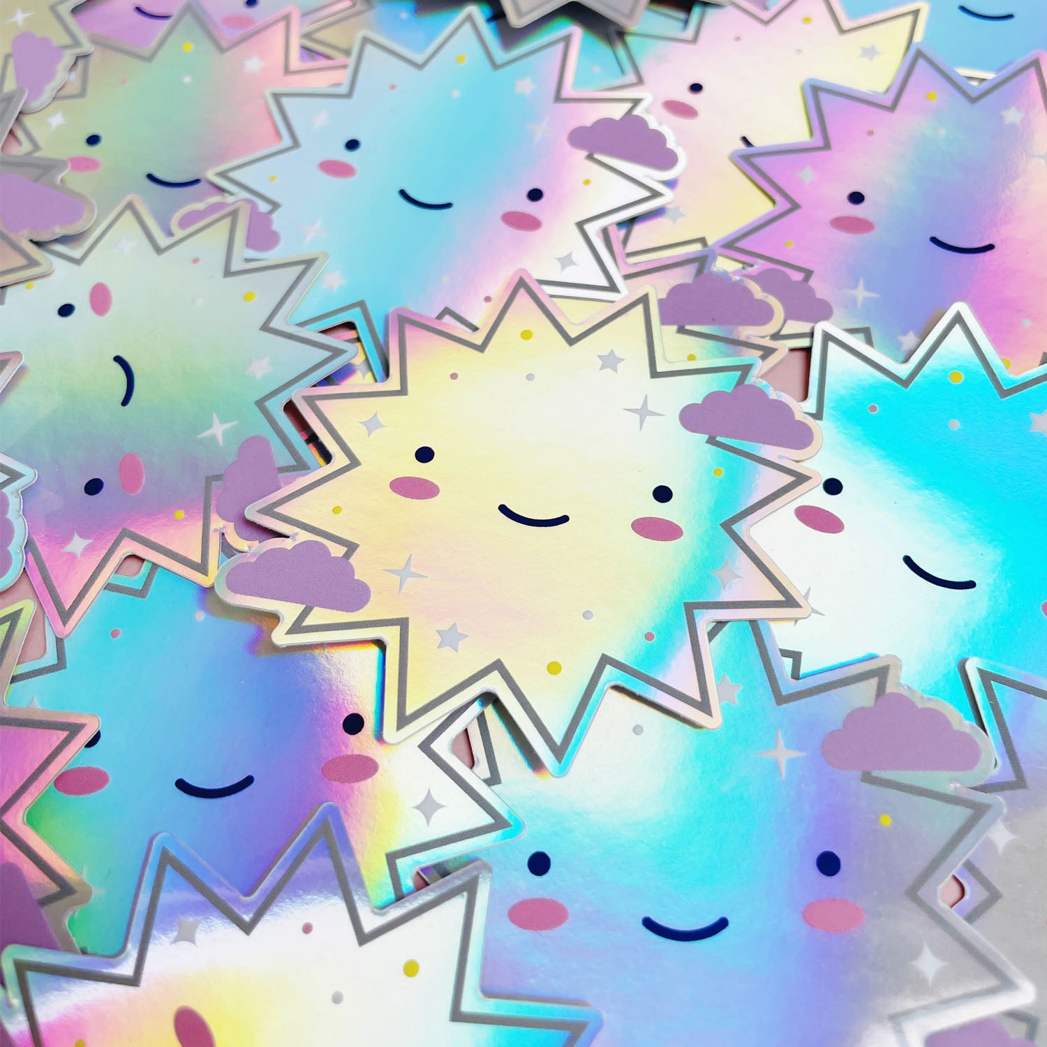 A pile of shiny iridescent holographic vinyl sticker featuring a smiling starburst. The surface is covered with dozens of the same design.