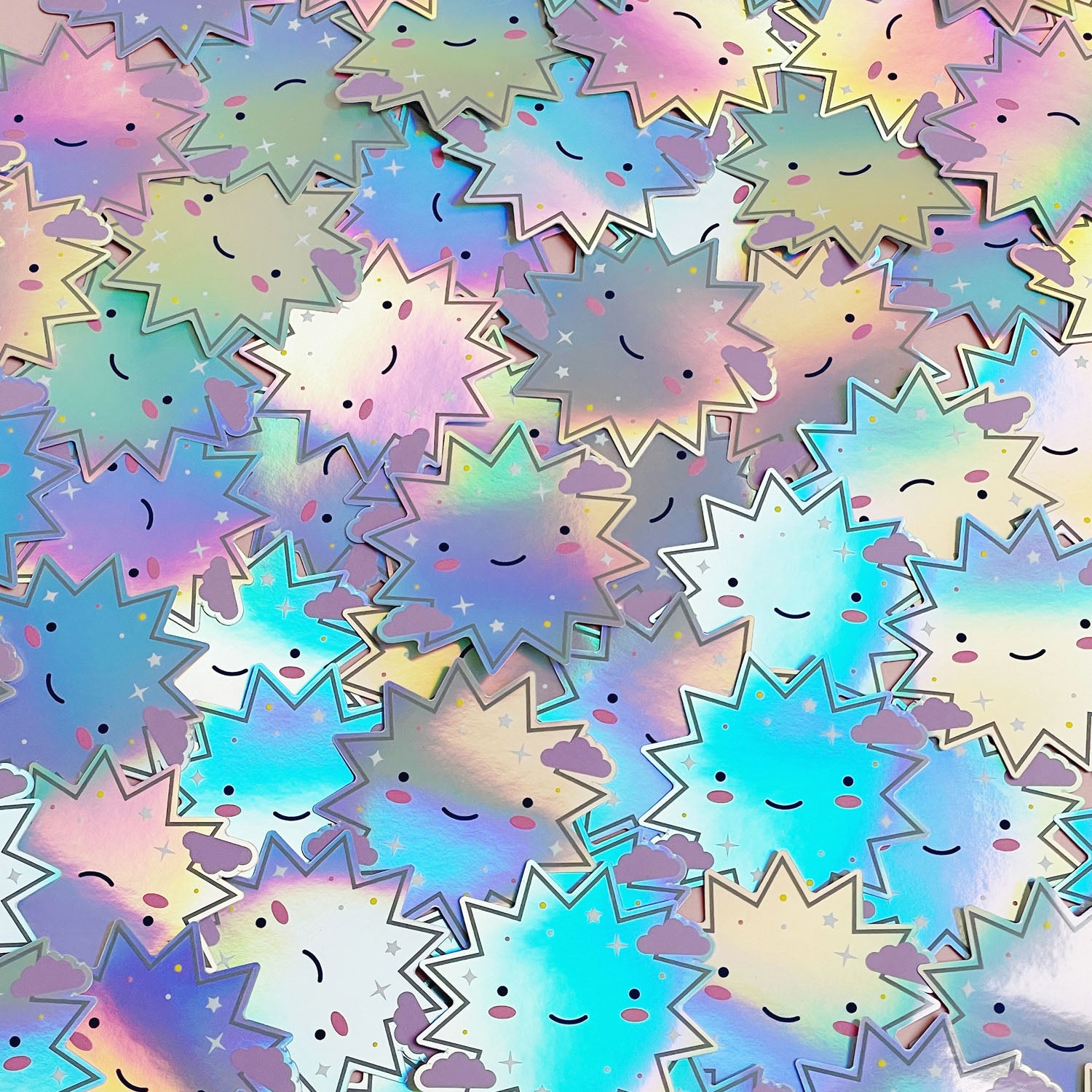 A pile of shiny iridescent holographic vinyl sticker featuring a smiling starburst. The surface is covered with dozens of the same design.