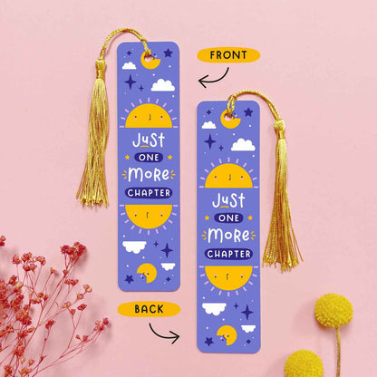 An image depicting the front and the back of the double sided metal bookmark which has been photographed on a pink background with dried flowers. Each bookmark has a gold tassel. The front and the back of the bookmark are printed with the same design of a sun, moon, stars and the hand drawn text that reads 'just one more chapter'.