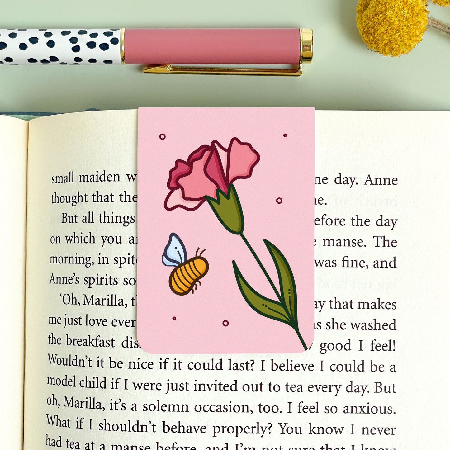 Pink carnation bookmark with a flower and bee design on an open book
