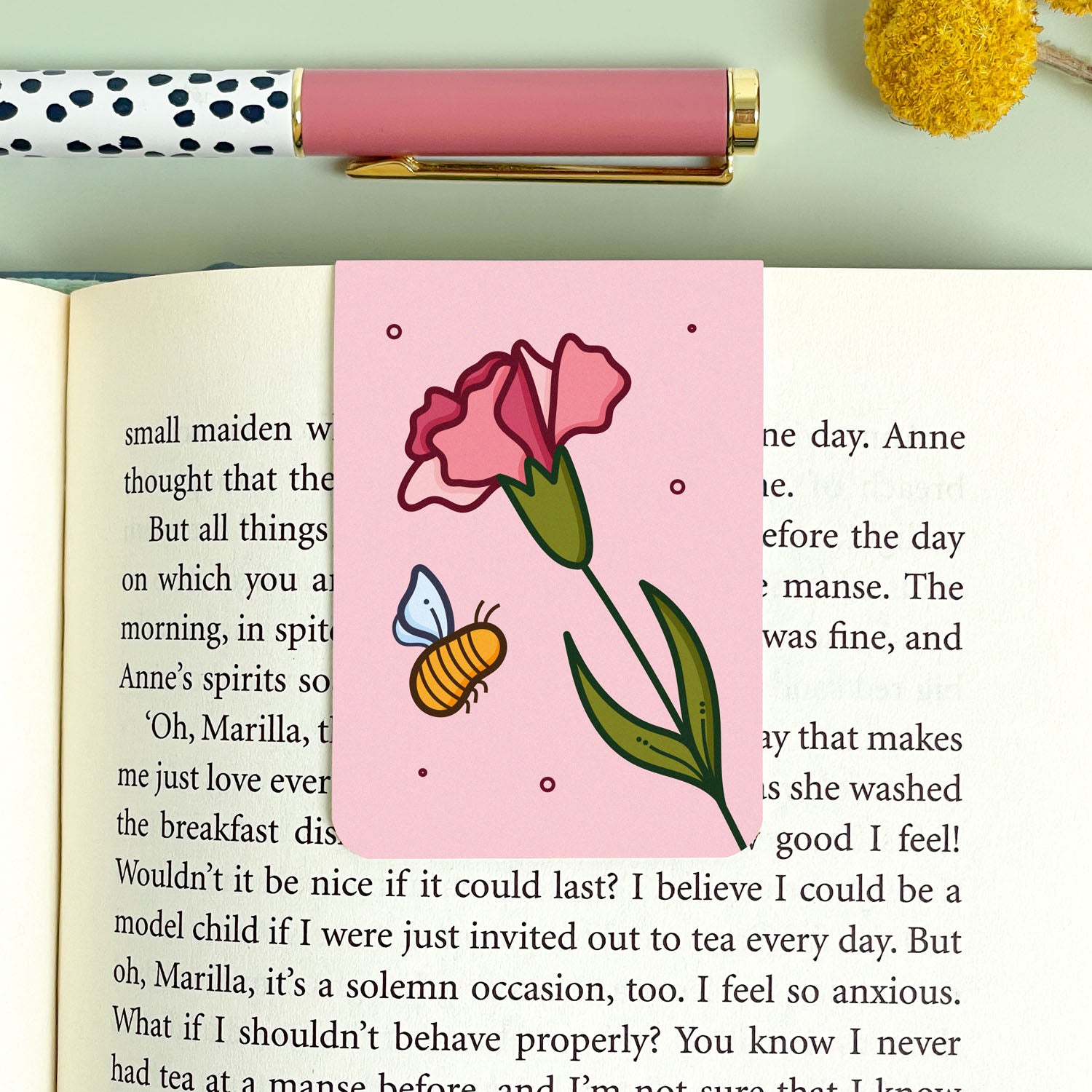 Pink carnation bookmark with a flower and bee design on an open book