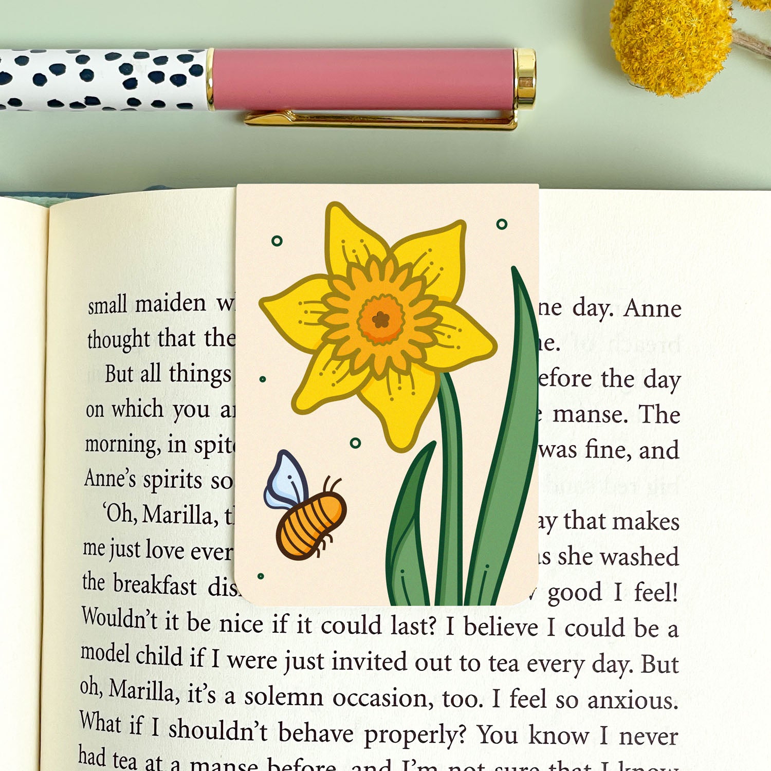 Bookmark with a yellow daffodil flower illustration and a pink pen on a green background