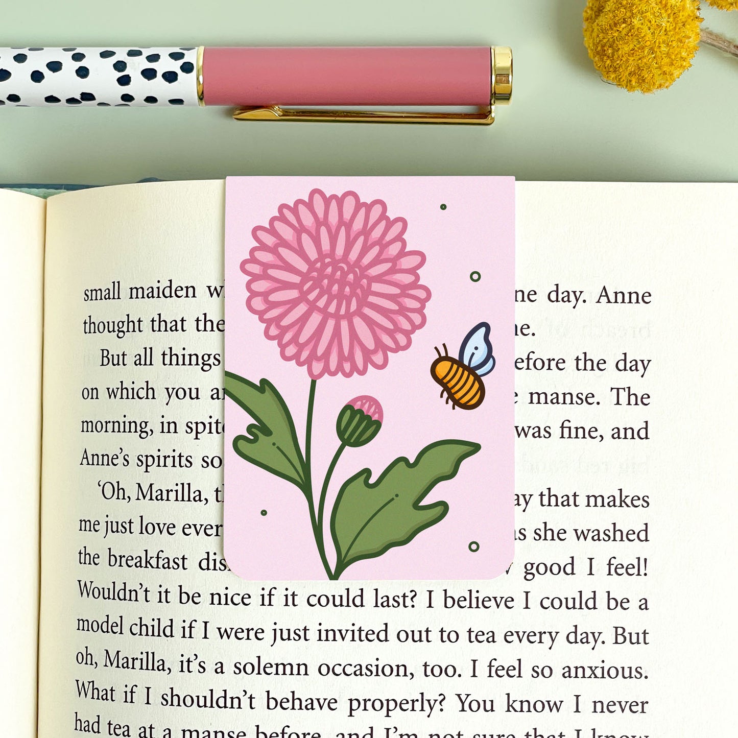 Floral chrysanthemum bookmark on an open book with a pen and decorative elements.