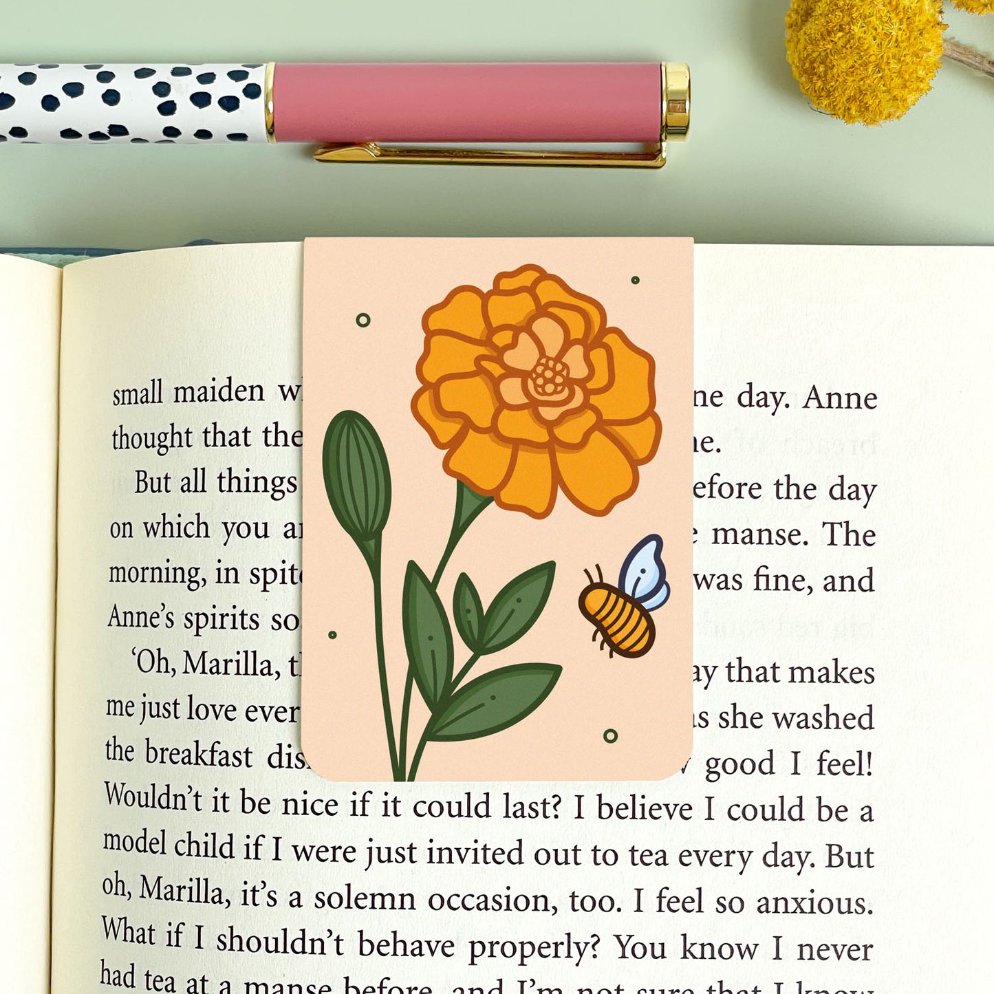 Floral marigold bookmark on an open book with a pen and decorative elements.
