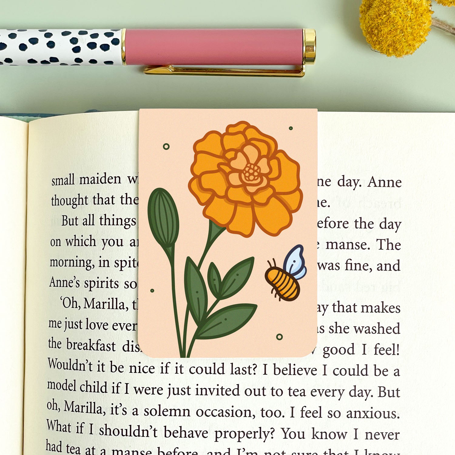 Floral marigold bookmark on an open book with a pen and decorative elements.