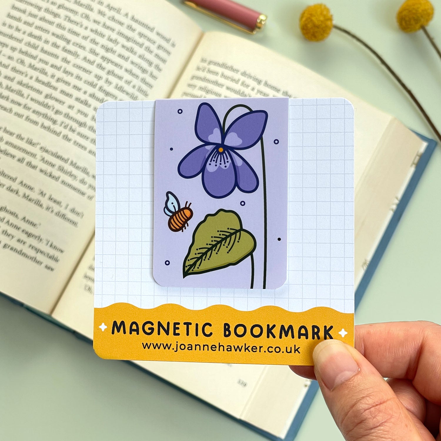 Magnetic bookmark with purple floral violet design held over an open book