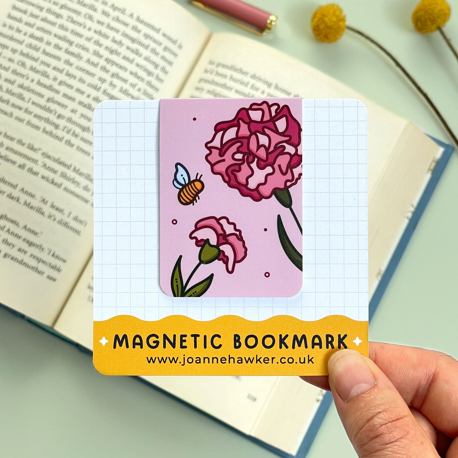 Magnetic bookmark with floral carnation design held over an open book