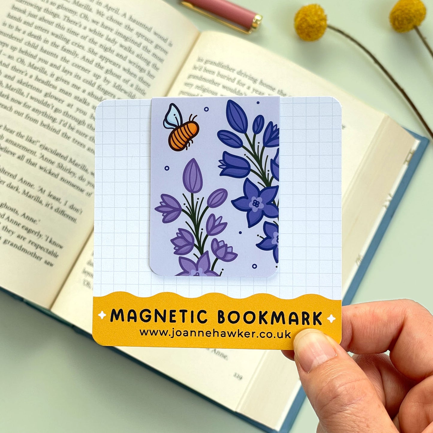 Magnetic bookmark with floral larkspur design held over an open book