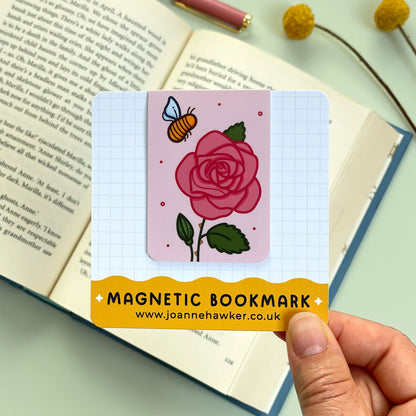 Magnetic bookmark with rose and bee design held over an open book.