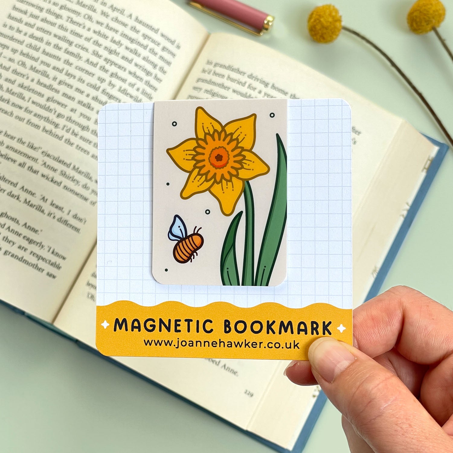 Magnetic bookmark with a daffodil design held over an open book.